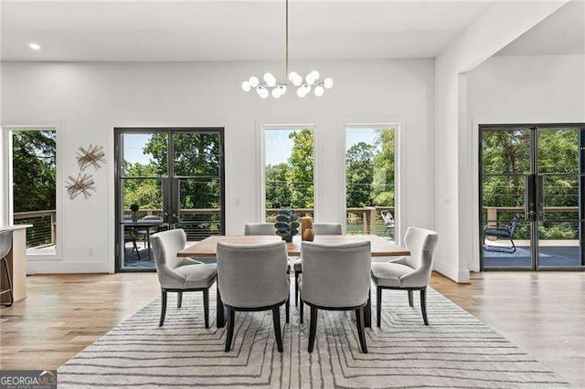 dining space featuring a healthy amount of sunlight, light hardwood / wood-style floors, french doors, and a chandelier