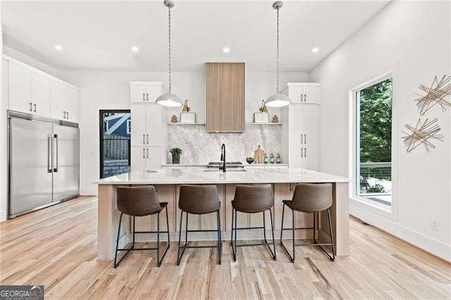 kitchen featuring hanging light fixtures, white cabinetry, stainless steel built in fridge, and a kitchen island with sink