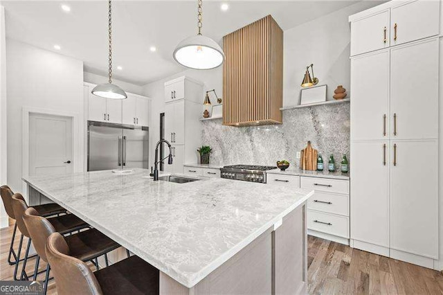 kitchen with white cabinetry, sink, built in fridge, and a center island with sink