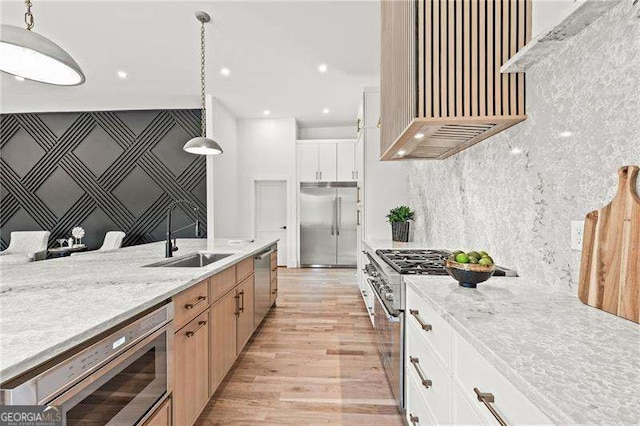 kitchen featuring sink, built in appliances, pendant lighting, light stone countertops, and white cabinets