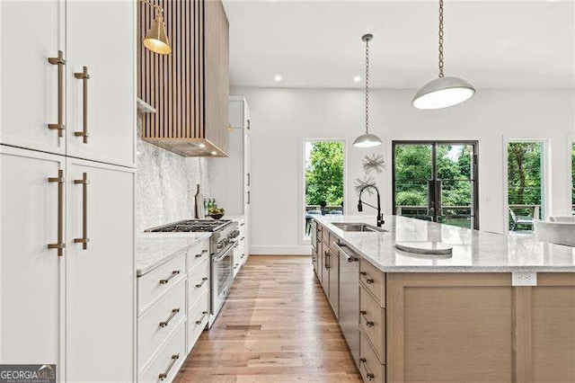 kitchen with sink, white cabinets, a large island with sink, stainless steel appliances, and light stone countertops