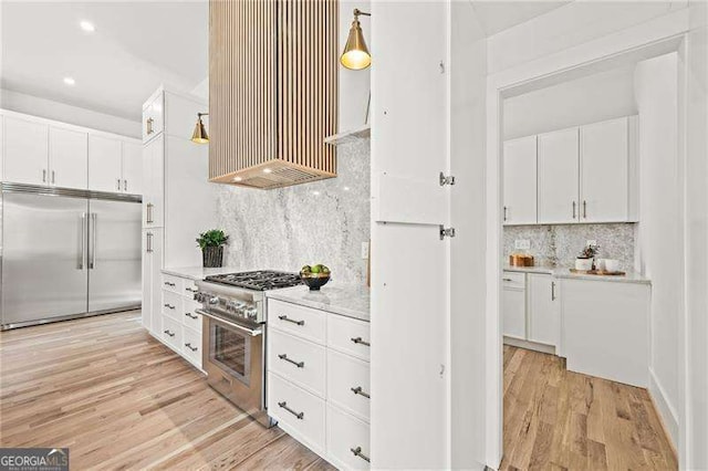 kitchen with white cabinetry, high quality appliances, decorative light fixtures, and light hardwood / wood-style flooring