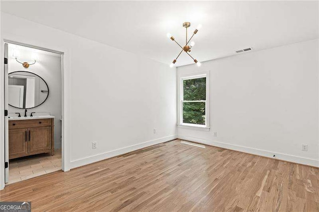 unfurnished bedroom featuring sink, a notable chandelier, light hardwood / wood-style flooring, and ensuite bath