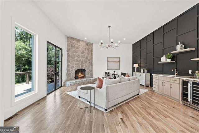 living room featuring an inviting chandelier, a stone fireplace, sink, and light wood-type flooring