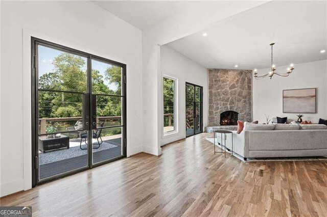 living room with a stone fireplace, a chandelier, light wood-type flooring, and french doors