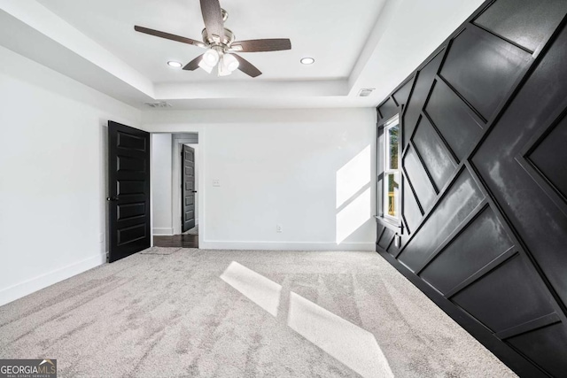 unfurnished room featuring light carpet, a tray ceiling, and ceiling fan