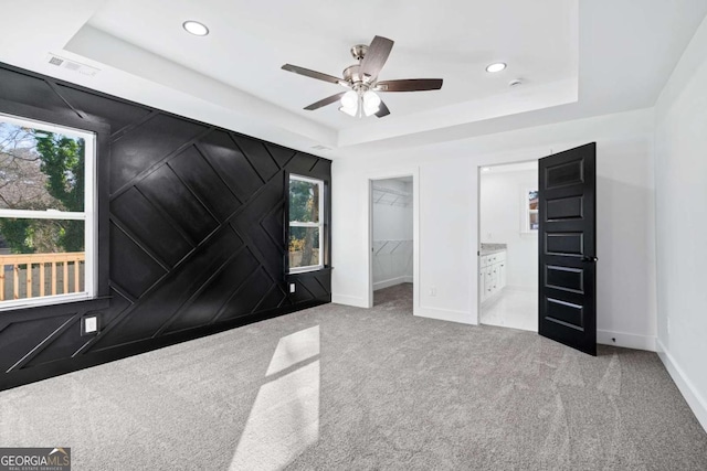 unfurnished bedroom featuring a walk in closet, a tray ceiling, and light colored carpet