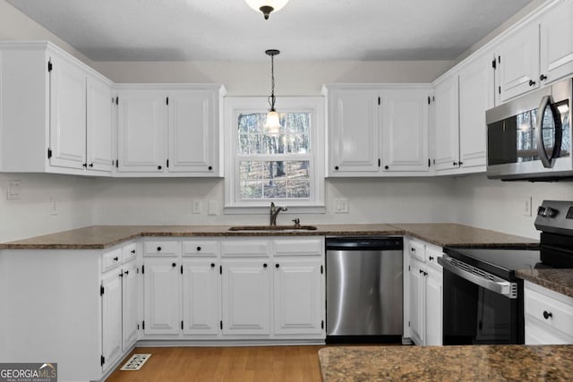 kitchen featuring sink, appliances with stainless steel finishes, white cabinetry, decorative light fixtures, and light wood-type flooring