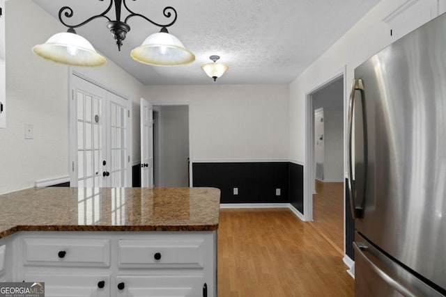 kitchen with white cabinetry, dark stone counters, stainless steel fridge, and decorative light fixtures