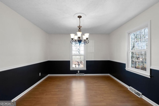 unfurnished dining area featuring wood-type flooring, plenty of natural light, a textured ceiling, and a chandelier