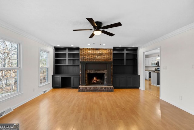 unfurnished living room featuring crown molding, built in features, ceiling fan, a fireplace, and light hardwood / wood-style floors