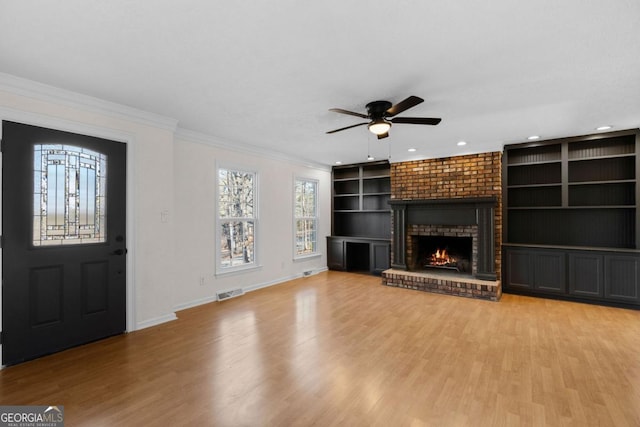 unfurnished living room with crown molding, a brick fireplace, built in features, and light hardwood / wood-style flooring