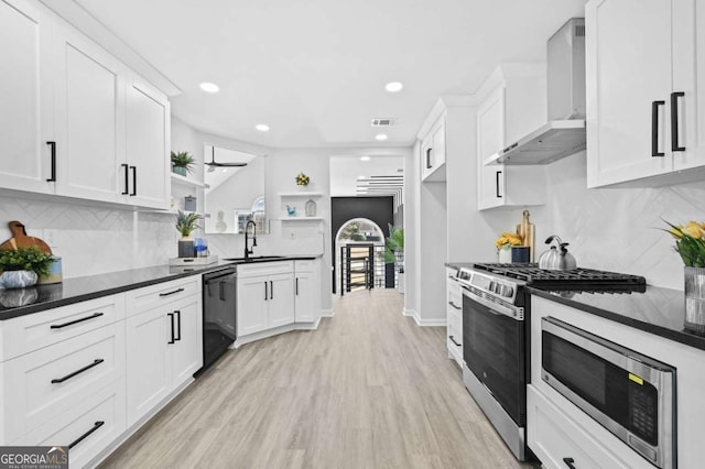 kitchen featuring white cabinetry, sink, wall chimney exhaust hood, stainless steel appliances, and light hardwood / wood-style flooring