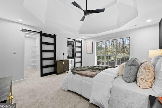 carpeted bedroom with a tray ceiling, a barn door, and ceiling fan