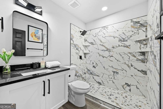 bathroom featuring a tile shower, vanity, hardwood / wood-style floors, and toilet