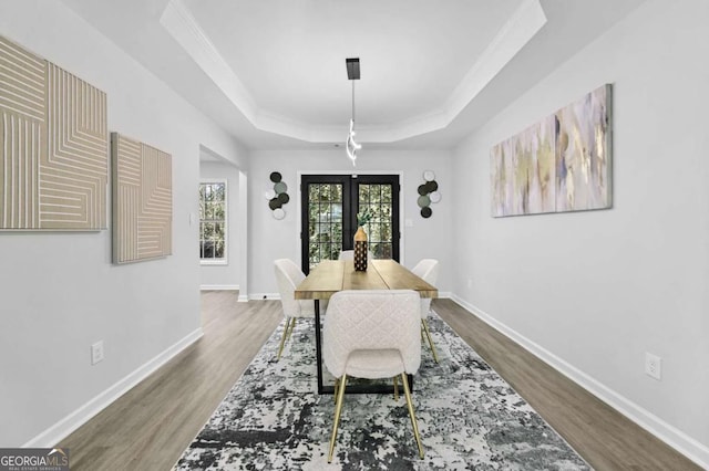 dining space with crown molding, wood-type flooring, a raised ceiling, and french doors