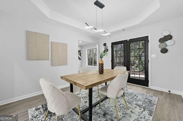 dining area with a raised ceiling, crown molding, hardwood / wood-style floors, and french doors