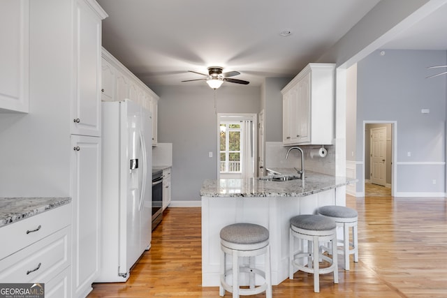 kitchen featuring sink, stainless steel range with electric cooktop, ceiling fan, white refrigerator with ice dispenser, and white cabinets