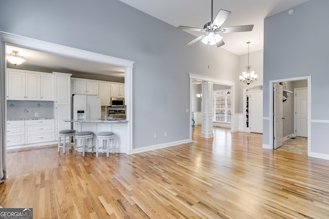 unfurnished living room with a high ceiling, ceiling fan with notable chandelier, and light wood-type flooring