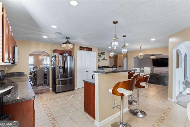 kitchen with a breakfast bar area, hanging light fixtures, stove, stainless steel refrigerator with ice dispenser, and a textured ceiling