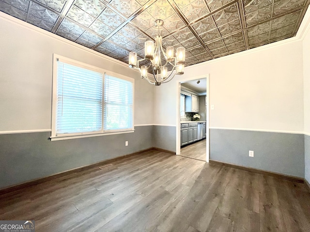 unfurnished dining area with wood-type flooring, crown molding, and an inviting chandelier