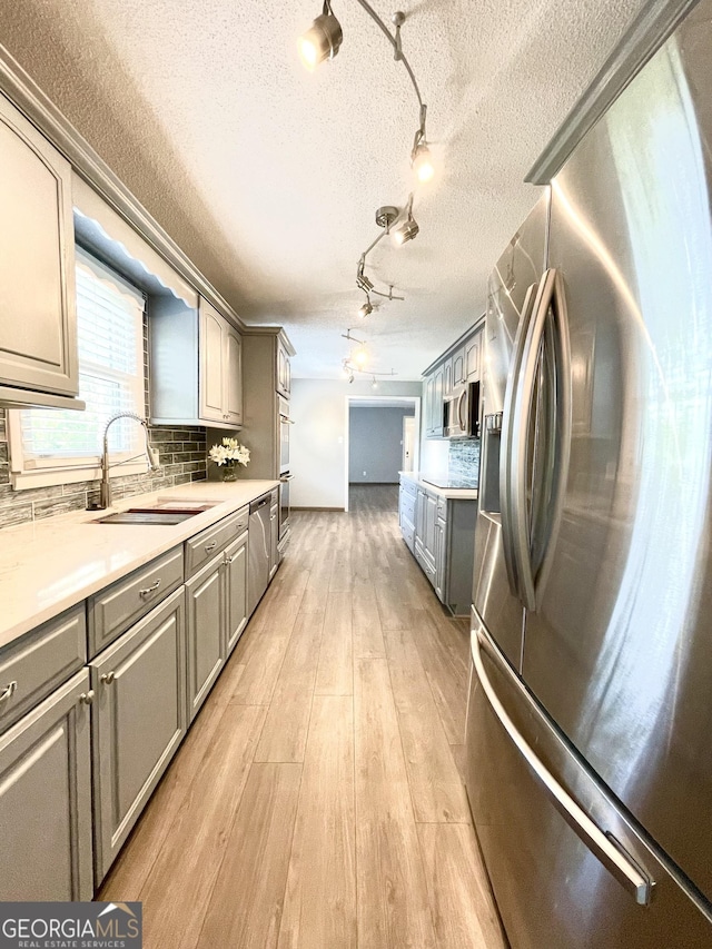 kitchen featuring gray cabinets, sink, backsplash, stainless steel appliances, and light wood-type flooring