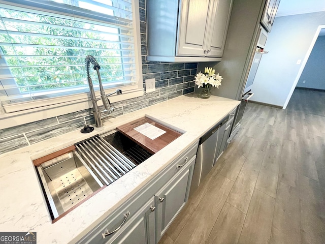 kitchen featuring sink, tasteful backsplash, light stone counters, light hardwood / wood-style flooring, and gray cabinets