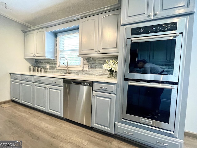 kitchen featuring gray cabinets, appliances with stainless steel finishes, sink, decorative backsplash, and light hardwood / wood-style flooring