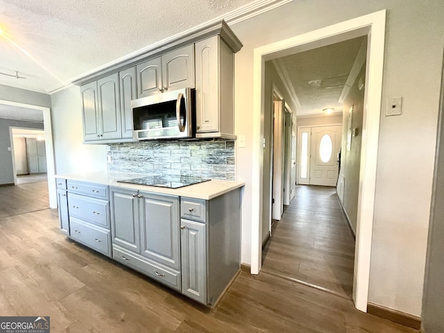 kitchen with ornamental molding, gray cabinets, hardwood / wood-style flooring, black electric stovetop, and backsplash