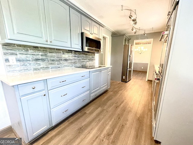 kitchen featuring tasteful backsplash, appliances with stainless steel finishes, an inviting chandelier, and light wood-type flooring