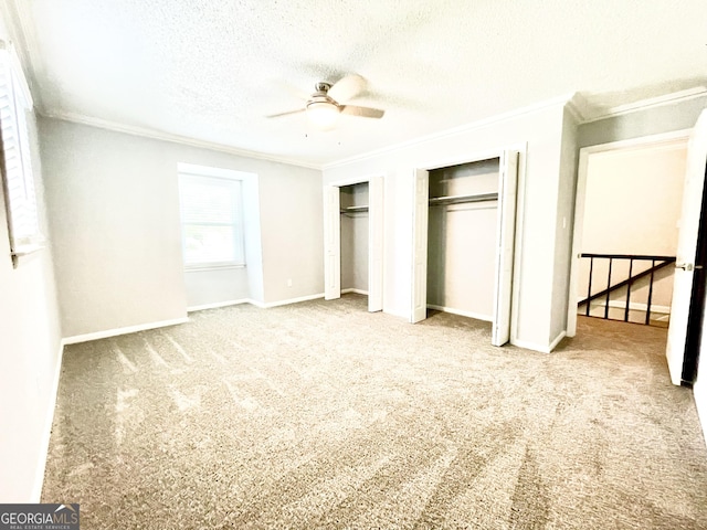 unfurnished bedroom with multiple closets, ornamental molding, carpet flooring, and a textured ceiling