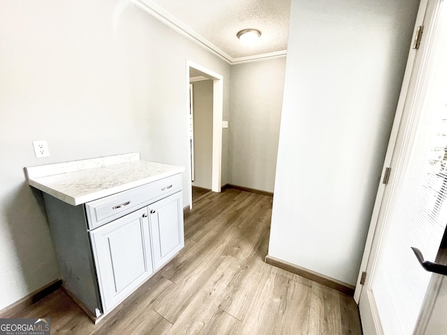 interior space featuring crown molding, a textured ceiling, light hardwood / wood-style flooring, and white cabinets