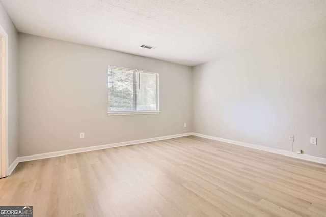 unfurnished room with light wood-type flooring, baseboards, visible vents, and a textured ceiling