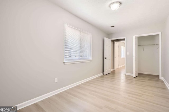 unfurnished bedroom with a closet, light wood finished floors, baseboards, and visible vents