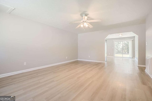 interior space featuring arched walkways, light wood-style flooring, a ceiling fan, and baseboards
