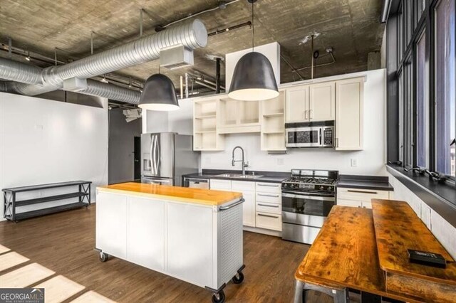 kitchen with dark wood-type flooring, sink, pendant lighting, stainless steel appliances, and white cabinets