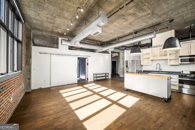 kitchen with pendant lighting, dark wood-type flooring, brick wall, and appliances with stainless steel finishes