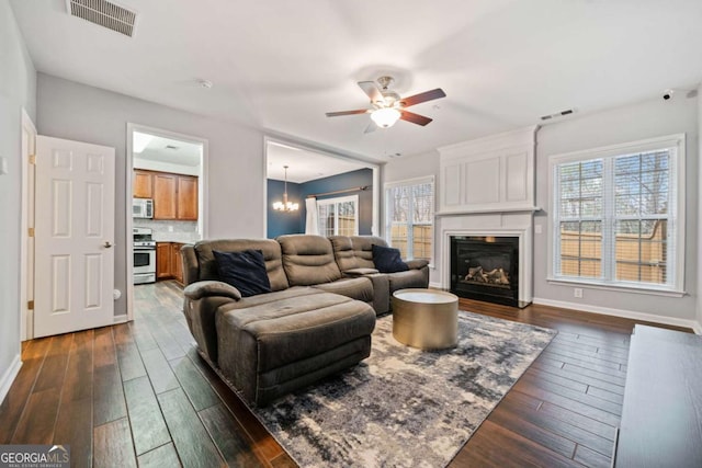 living room with plenty of natural light, ceiling fan with notable chandelier, and dark hardwood / wood-style flooring