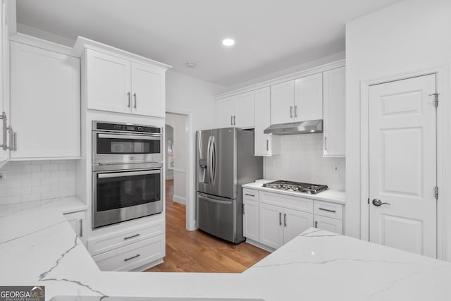 kitchen with white cabinetry, light stone counters, stainless steel appliances, and hardwood / wood-style flooring