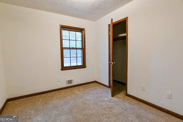 unfurnished bedroom featuring a spacious closet, light carpet, a textured ceiling, and a closet