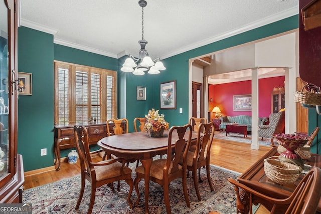 dining room with a textured ceiling, crown molding, wood finished floors, decorative columns, and an inviting chandelier