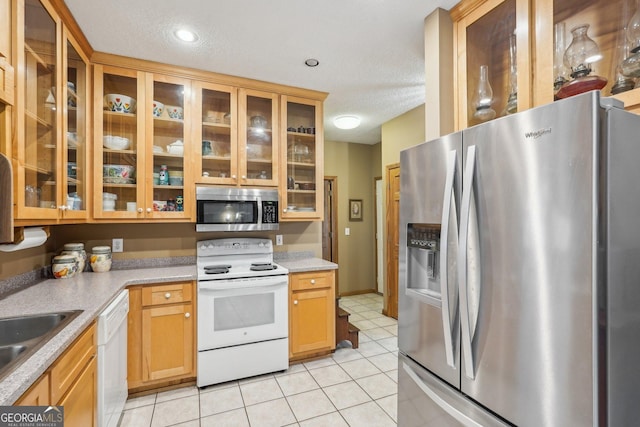 kitchen with light tile patterned floors, a textured ceiling, light countertops, appliances with stainless steel finishes, and glass insert cabinets