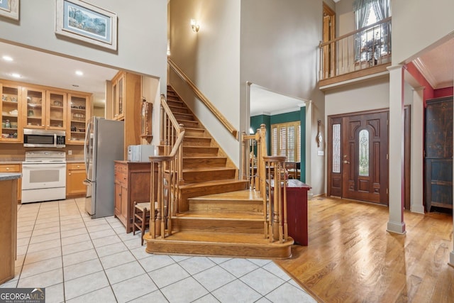 foyer entrance with crown molding, a high ceiling, light hardwood / wood-style flooring, and ornate columns