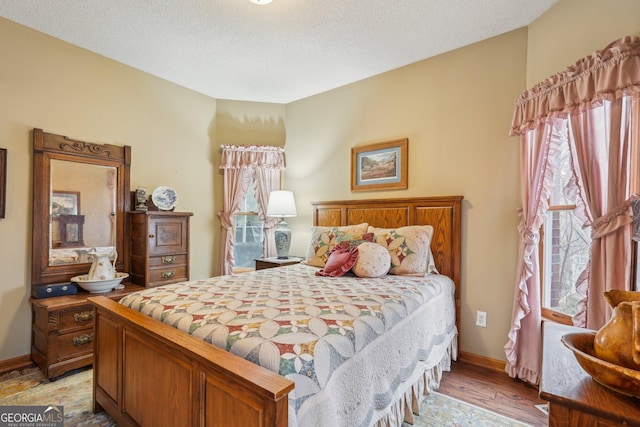 bedroom with light wood-type flooring, baseboards, and a textured ceiling