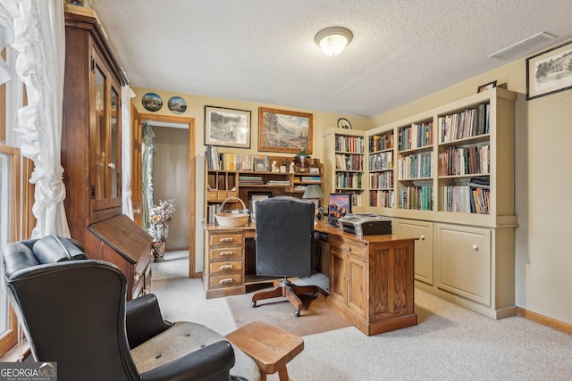 office area with a textured ceiling, baseboards, visible vents, and light colored carpet