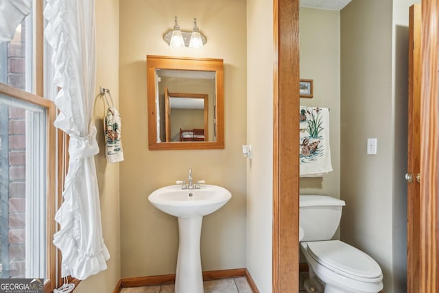 half bathroom with baseboards, a sink, toilet, and tile patterned floors