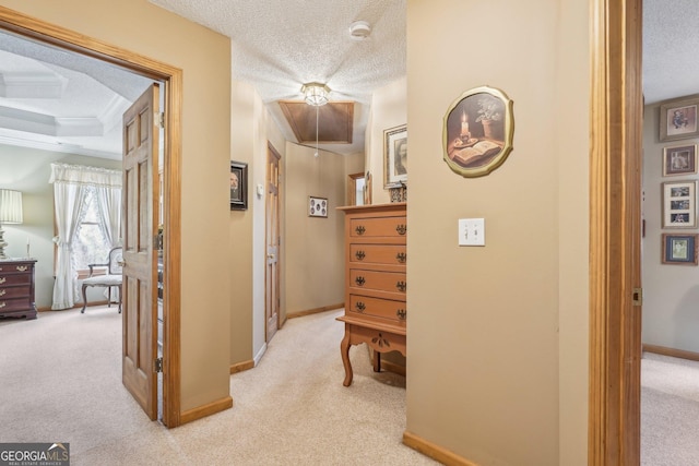 hall with attic access, baseboards, a textured ceiling, and light colored carpet