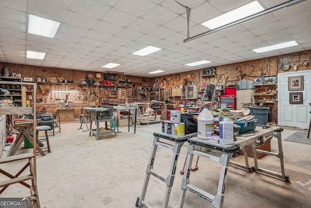 miscellaneous room featuring wood walls, concrete floors, a drop ceiling, and a workshop area