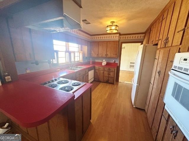 kitchen featuring white appliances, range hood, a textured ceiling, kitchen peninsula, and light wood-type flooring