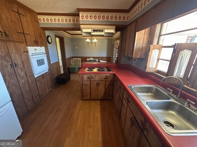 kitchen with stovetop, sink, wood-type flooring, a notable chandelier, and oven